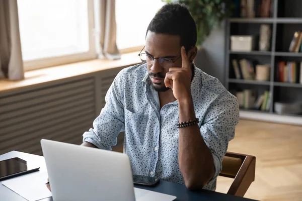 Pensativo e duvidoso empresário afro-americano olhando para a tela do laptop — Fotografia de Stock