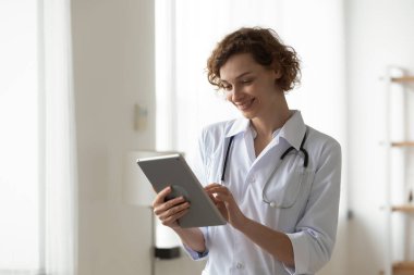 Gülümseyen kadın profesyonel doktor dijital tablet kullanıyor, ofiste duruyor.