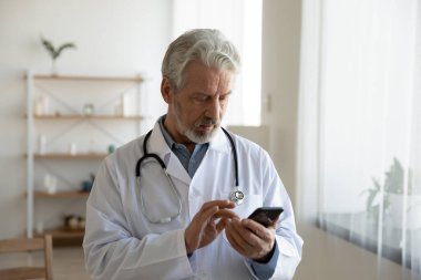 Ciddi odaklı yetişkin doktor telefon kullanarak, ekrana bakarak