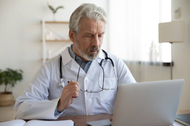 Ciddi bir yetişkin doktor gözlüğünü çıkarıp bilgisayar ekranına bakıyor.