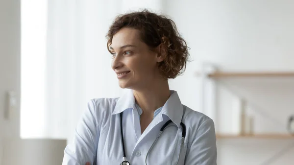 Close-up glimlachende dromerige jonge vrouw arts kijken naar venster — Stockfoto
