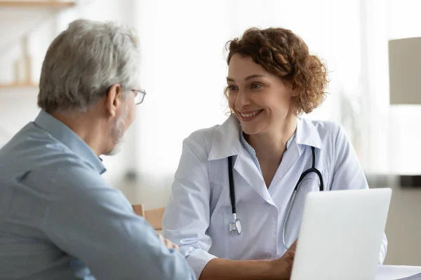 Smiling woman doctor listening to mature patient complaints at meeting