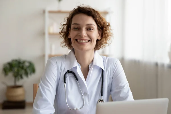 Huvudskott porträtt leende kvinna läkare sitter vid skrivbordet — Stockfoto