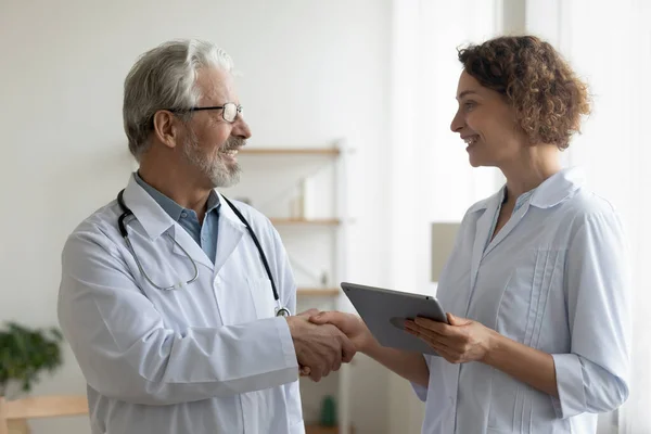 Smiling mature doctor shaking young nurse hand, thanking for help — Stock Photo, Image