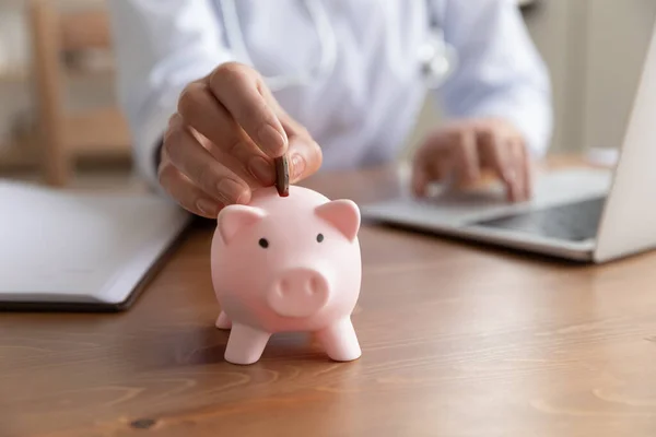 Primer plano joven doctora poner moneda en alcancía — Foto de Stock