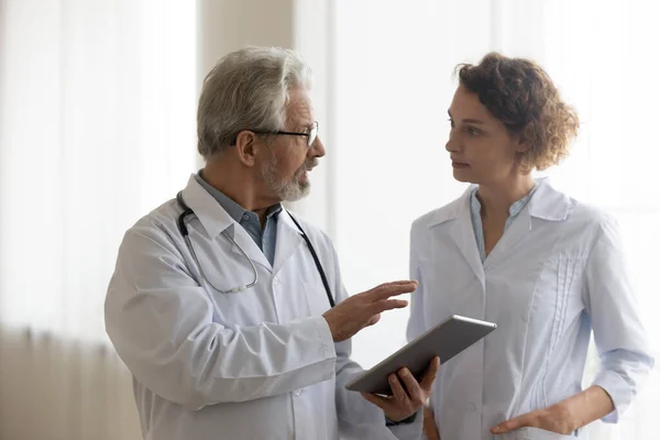 Ernste reife Ärztin und junge Krankenschwester reden und arbeiten zusammen — Stockfoto