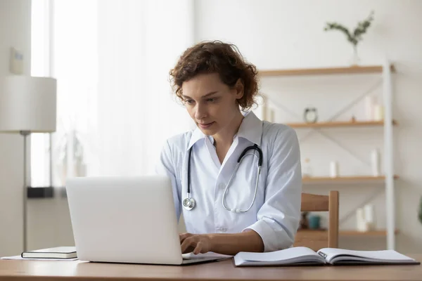 Serieuze vrouw arts werken op laptop, zitten aan het bureau — Stockfoto
