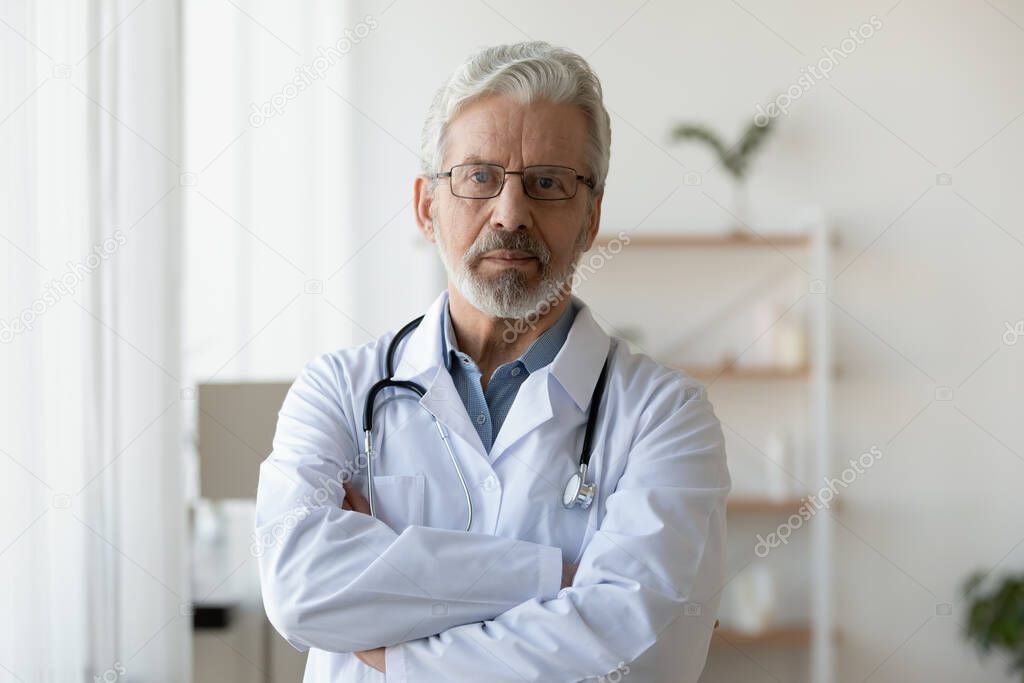 Head shot portrait mature doctor wearing glasses standing in office