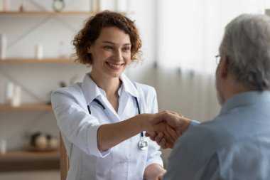 Gülümseyen dost canlısı doktor toplantıda olgun hasta elini sıkıyor.