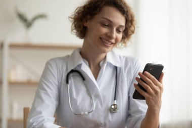 Gülümseyen kadın doktor video görüşmesi yapıyor, elinde akıllı telefon var.