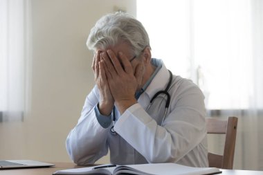 Stresli olgun doktor elleriyle yüzünü kapatıyor.
