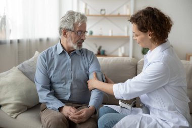 Genç hemşire evde hasta tansiyonunu ölçüyor.