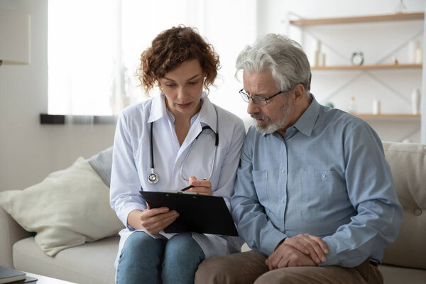 Young woman doctor nurse consulting mature patient during homecare visit