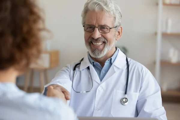 Close up smiling mature doctor shaking female patient hand — Stock Photo, Image