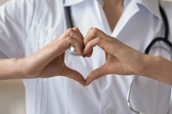 Cerca de la mujer joven con uniforme médico mostrando el gesto del corazón — Foto de Stock