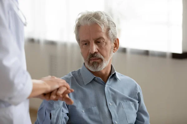 Nahaufnahme junge Krankenschwester tröstet depressive reife Patientin und hält Hände — Stockfoto