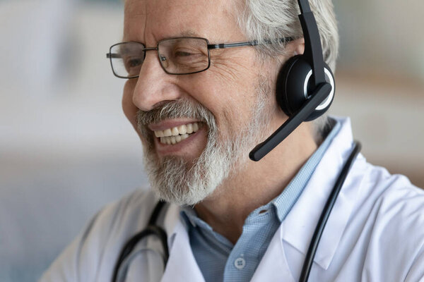 Close up smiling mature doctor wearing headset working online