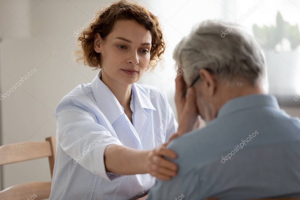Caring young woman doctor comforting depressed mature patient at meeting
