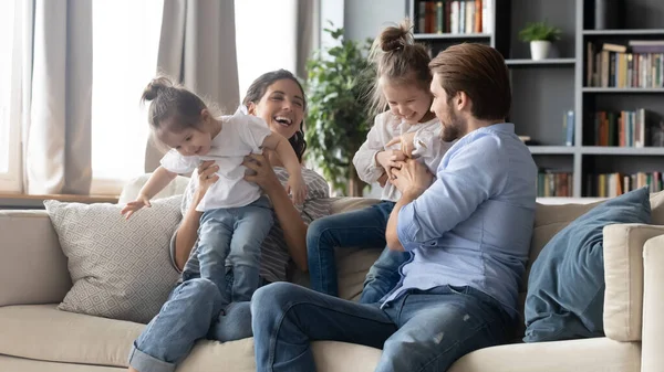 Joyful carefree parents playing with adorable little kids on sofa. — Stock Photo, Image