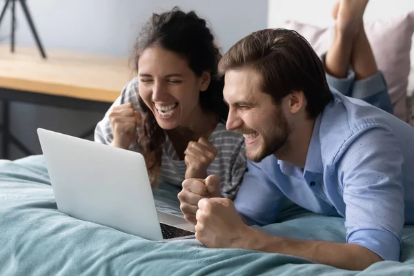 Overjoyed young couple lying on bed, looking at laptop screen. — Stock Photo, Image