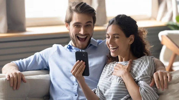 Emotionele jonge dolblij paar op zoek naar smartphone scherm. — Stockfoto