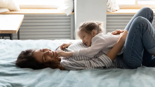 Happy young mommy lying with little baby girl on bed. — Stock Photo, Image