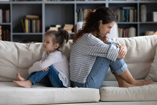 Unhappy little girl sitting back to back with stressed mother.