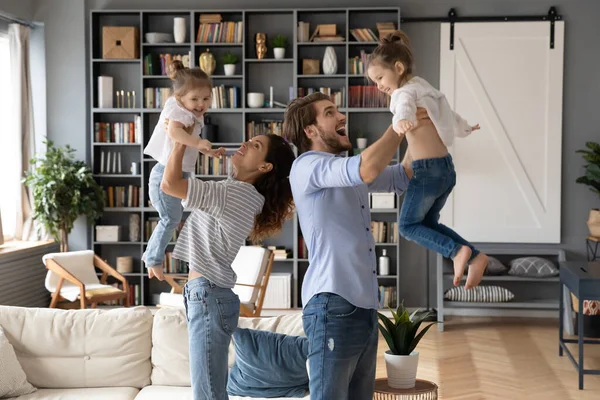 Glückliches junges tatkräftiges Paar hebt kleine lachende Kinder in die Luft. — Stockfoto