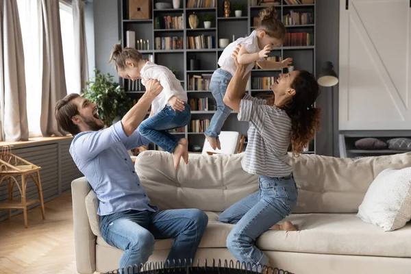 Jeune couple parents levant sur les bras joyeuses filles riantes. — Photo