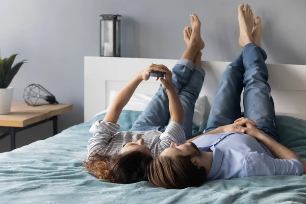 Ontspannen jong paar liggend op bed, poseren voor selfie op smartphone. — Stockfoto