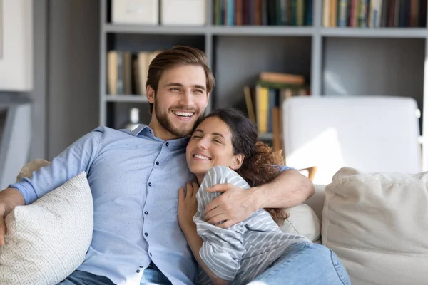 Happy young married couple embracing relaxing on sofa. — Stock Photo, Image