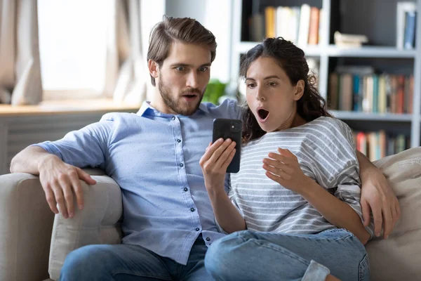 Geschocktes Familienpaar blickt mit offenem Mund auf Handybildschirm. — Stockfoto