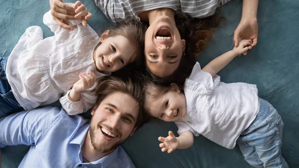 Gelukkig jonge ouders ontspannen op bed met vreugdevolle kleine dochters. — Stockfoto