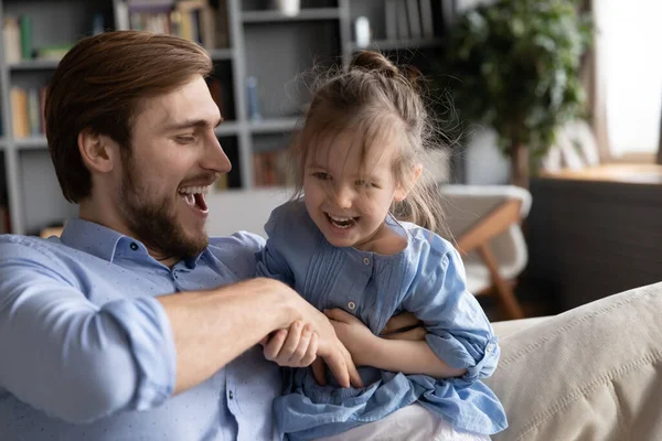 Sorrindo pai cócegas engraçado bebê menina, se divertindo no sofá. — Fotografia de Stock