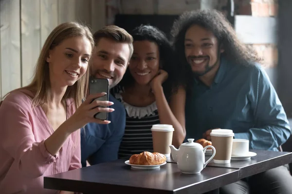 Щасливі різноманітні друзі беруть селфі, сидячи за столом у кафе — стокове фото