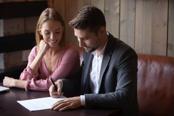 Happy young couple making deal, husband signing contract at meeting — Stock Photo, Image
