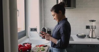 Hintli bir kadın akıllı telefon hazırlıyor. Yemek tarifi yöneticisi uygulamaları kullanıyor.