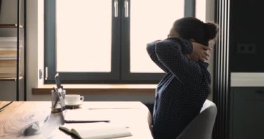 Kadın defter üzerinde çalışırken ellerini başının arkasına koyar.