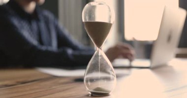 Dizüstü bilgisayarda çalışan iş kadını zaman aralığını gösteren kum saatine odaklanıyor