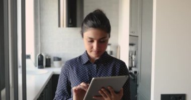 Tablet cihazı kullanan Hintli kadın kameraya bakıp gülümsüyor.