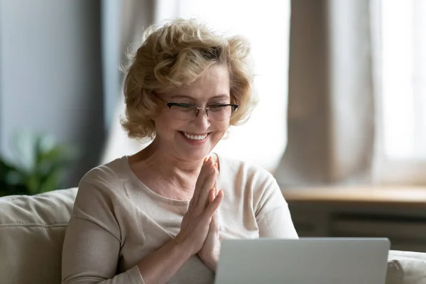 Sorridente donna matura con gli occhiali che legge buone notizie, utilizzando il computer portatile — Foto Stock