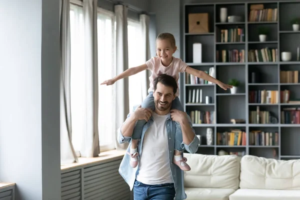 Улыбающийся молодой отец держит милую маленькую дочь, притворяющуюся летающей — стоковое фото