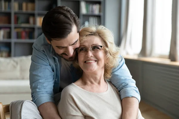 Glücklicher junger Mann umarmt reife Mutter mit Brille von hinten — Stockfoto