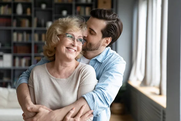 Liebevoll erwachsener Sohn küsst und umarmt glücklich reife Mutter — Stockfoto