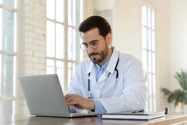Konzentrierte junge Ärztin mit Brille arbeitet im Büro am Laptop — Stockfoto