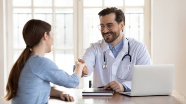 Üniformalı gülümseyen genç doktor hasta kadının elini sıkıyor.