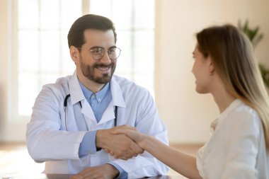 Toplantıda gülümseyen doktor hasta elini sıkıyor.