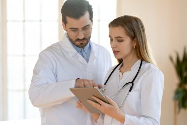 Kendine güvenen doktor ve genç hemşire konuşuyor, birlikte çalışıyorlar, tablet kullanıyorlar.