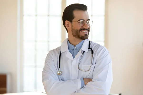 Smiling dreamy young man doctor wearing glasses looking to aside — Stock Photo, Image