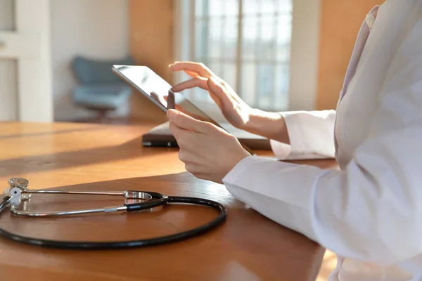 Primer plano mujer médico sosteniendo la tableta, sentado en la mesa — Foto de Stock